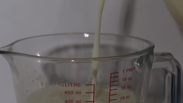 Dzbanek mleka w szklance pomiarowej dzbanek biały tło średni zoom strzał selektywny ostrość - Materiał filmowy, wideo