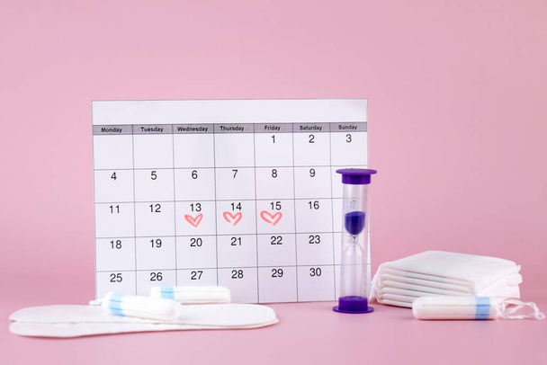 Damskie poduszki miesiączkowe, tampony, kalendarz menstruacji kobiet i budzik na różowym tle. Okres krytycznych dni. Miejsce na tekst. - Zdjęcie, obraz