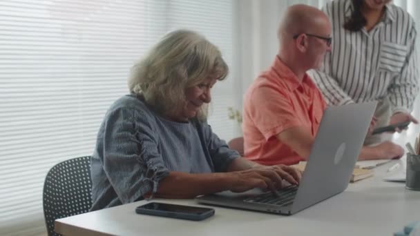 Keskikokoinen muotokuva iloinen kypsä nainen oppii käyttämään kannettavaa tietokonetta ja katsot kameraa istuu vieressä mies luokkatoveri - Materiaali, video