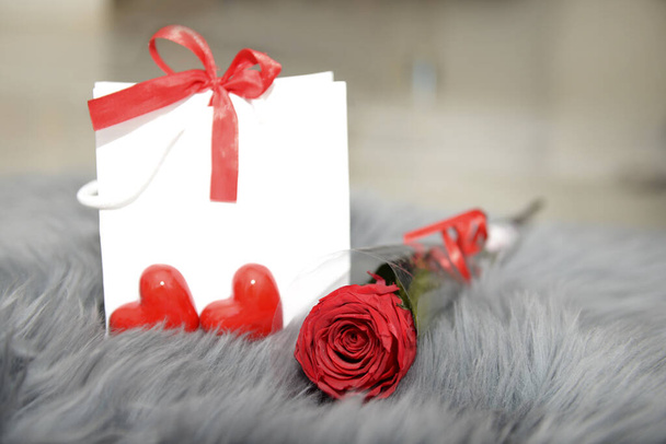 Εορταστικό φόντο από τσάντα δώρο με τόξο, σταθεροποιημένο τριαντάφυλλο και καρδιές σε γκρι γούνα για την ημέρα του Αγίου Βαλεντίνου, ημέρα της μητέρας, γενέθλια. - Φωτογραφία, εικόνα