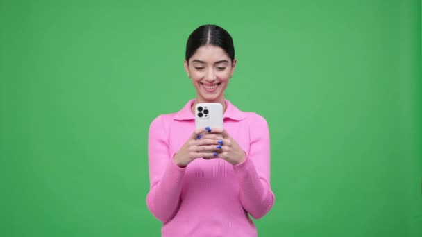 Spokojenost kavkazské mladé ženy relaxovat s mobilním telefonem, textové zprávy, surfování na internetu a směje se na zeleném pozadí. Online zábavní koncept. - Záběry, video
