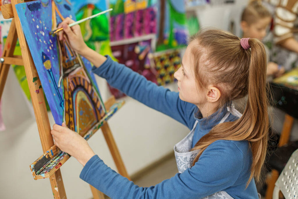 Mladá dívka s culíkem, hluboce koncentrovaná při malování barevného obrazu na plátno během umělecké třídy - Fotografie, Obrázek