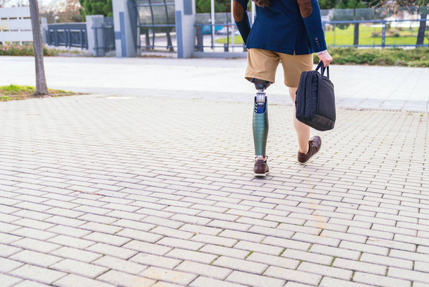 Un hombre de negocios irreconocible con una pierna artificial caminando rápidamente por una pasarela de adoquines, centrado en su viaje por delante - Foto, imagen
