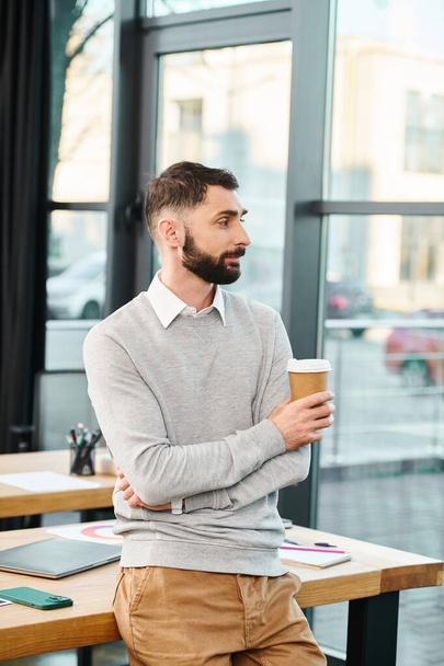 Egy férfi ül egy asztalnál, csendben élvezi egy csésze kávét egy modern irodai környezetben. - Fotó, kép