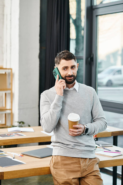 Ένας άνθρωπος σε ένα επιχειρηματικό περιβάλλον κρατά ένα φλιτζάνι καφέ, ενώ μιλάμε σε ένα κινητό τηλέφωνο. - Φωτογραφία, εικόνα