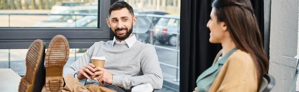 Un hombre se sienta en una silla, sosteniendo una taza de café, profundamente en el pensamiento en un ambiente de oficina corporativa. - Foto, Imagen