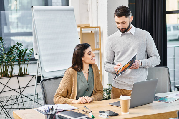 Een man en vrouw voeren een productieve discussie terwijl ze aan een tafel zitten met een laptop in een kantooromgeving. - Foto, afbeelding