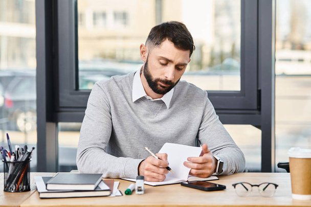 Ένας άνθρωπος σε ένα εταιρικό γραφείο επιμελώς γράφει σε ένα κομμάτι χαρτί στο γραφείο του, βυθισμένος στον κόσμο των λέξεων. - Φωτογραφία, εικόνα