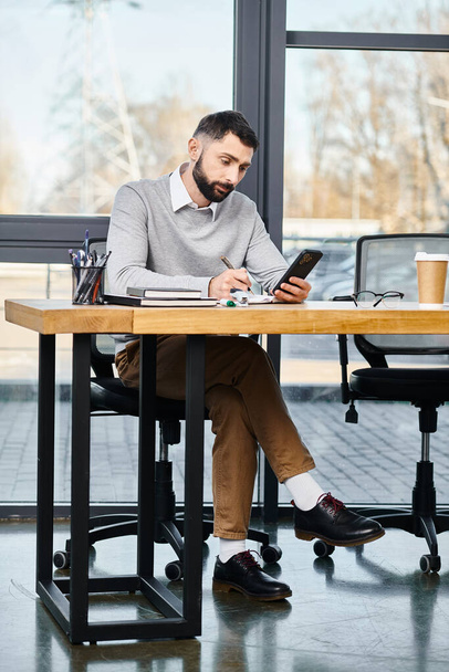 Egy férfi belemerül a mobiljába egy asztalnál egy irodai környezetben, egy vállalati kultúra része.. - Fotó, kép