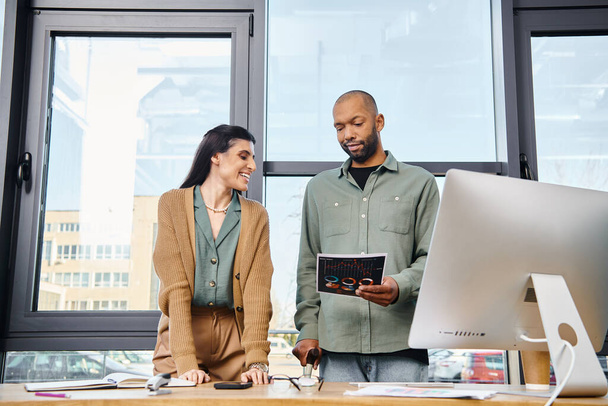 Ένας άντρας και μια γυναίκα συνεργάζονται σε ένα γραφείο, στέκονται μπροστά σε έναν υπολογιστή, δουλεύοντας μαζί σε ένα επιχειρηματικό σχέδιο.. - Φωτογραφία, εικόνα