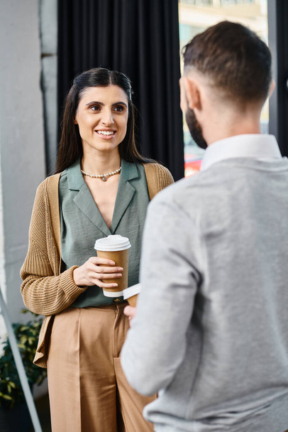 Una donna e un uomo chiacchierano casualmente mentre lui tiene una tazza di caffè in un ambiente di ufficio. - Foto, immagini