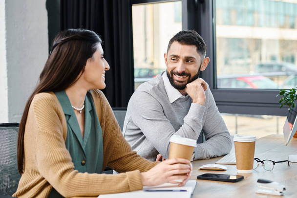 Un hombre y una mujer entablando una conversación reflexiva en una mesa, inmersos en una profunda discusión en un entorno de oficina. - Foto, Imagen
