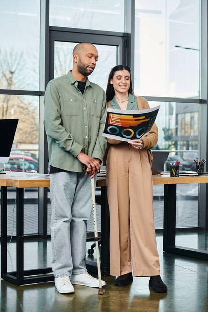 Άνδρας με ειδικές ανάγκες και γυναίκα στέκονται μαζί σε ένα επιχειρηματικό γραφείο, συζητώντας ένα έργο ως μέρος της εταιρικής κουλτούρας. - Φωτογραφία, εικόνα