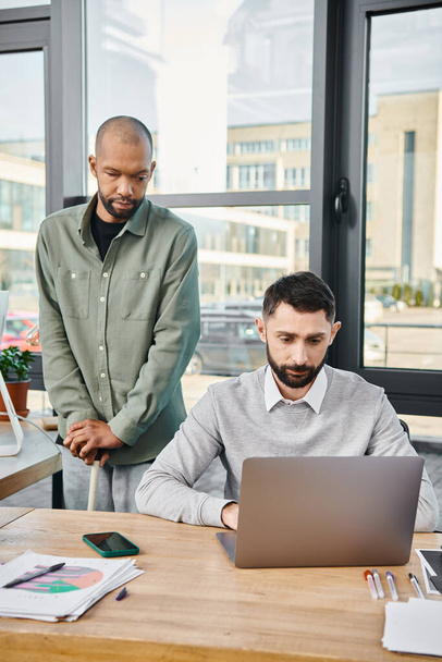 Dos hombres de negocios en una oficina que participan con un ordenador portátil, sus rostros reflexivos y enfocados, en medio de una sesión de trabajo productivo. - Foto, Imagen