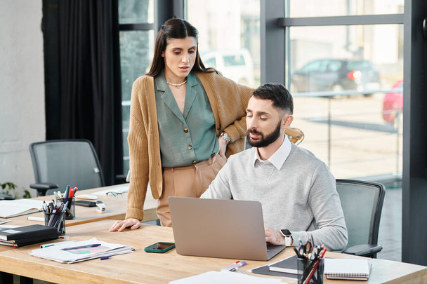 Ein Mann und eine Frau führen eine produktive Diskussion, während sie in einem modernen Büroumfeld auf einen Laptop blicken. - Foto, Bild