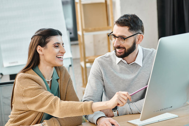Un homme et une femme heureux assis à une table, immergés dans leur travail sur un ordinateur portable, incarnant une culture d'entreprise dynamique. - Photo, image