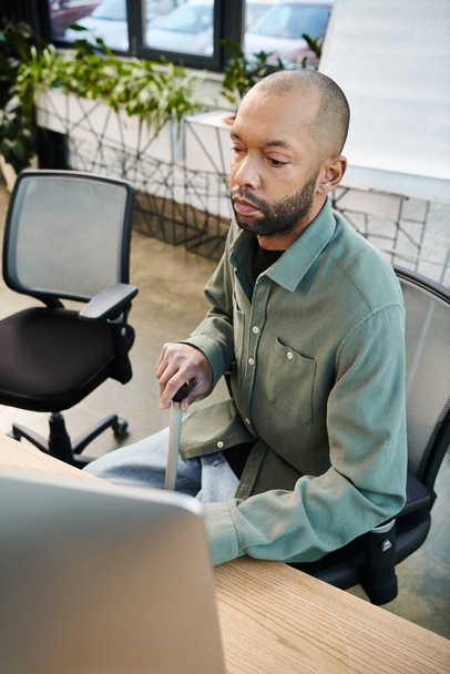Afro-Amerikaanse gehandicapte man met myasthenia gravis voor een laptop, gericht op werk in een bruisende kantooromgeving vol bedrijfscultuur. - Foto, afbeelding
