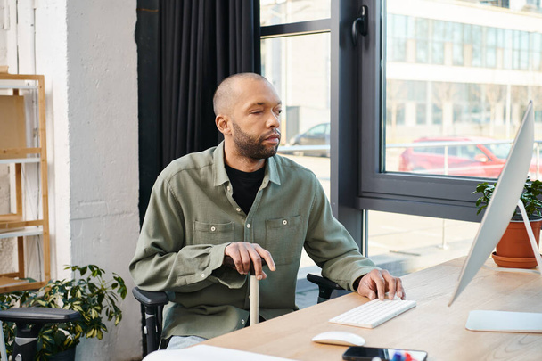 Un homme afro-américain handicapé atteint de myasthénie grave s'est concentré sur son écran d'ordinateur, tapant sur un clavier, créant un projet numérique dans un cadre de bureau d'entreprise. - Photo, image