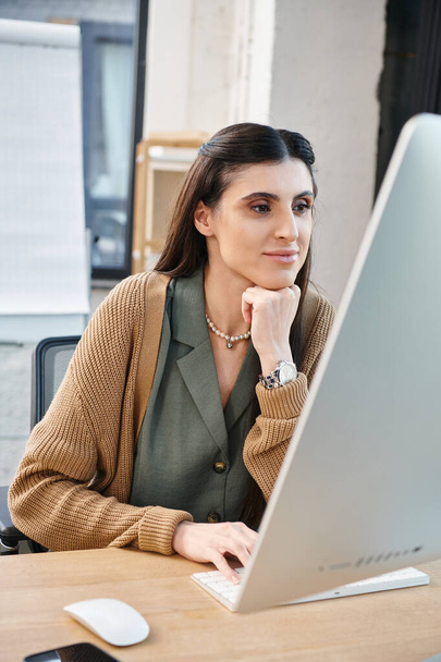 Una donna assorta nel lavoro, seduta davanti al suo computer portatile in un ufficio aziendale. - Foto, immagini
