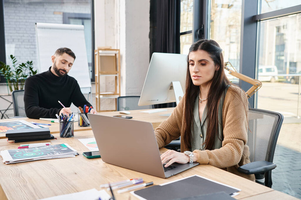 Egy férfi és egy nő ül az asztalnál, mélyen dolgoznak a laptopokon, testesítik meg a csapatmunka lényegét egy vállalati környezetben.. - Fotó, kép