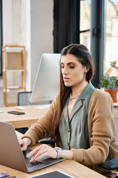 Een vrouw gefocust op haar laptop, diep bezig met kantoorwerk aan een bureau in een zakelijke setting. - Foto, afbeelding