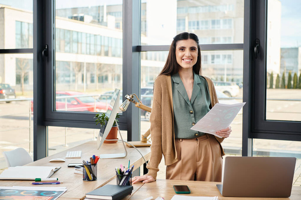 Egy profi nő áll egy íróasztalnál egy laptoppal, elmerülve egy vállalati projektben egy modern irodai környezetben.. - Fotó, kép