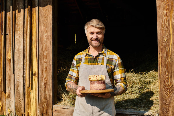 joyous handsome farmer with tattoos holding homemade cheese in his hands and smiling at camera - Foto, imagen