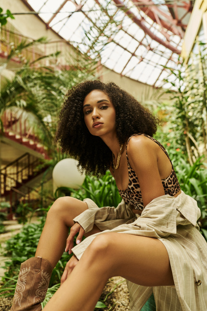 young african american woman with curly hair posing in her trendy look in a botanical setting - Photo, Image