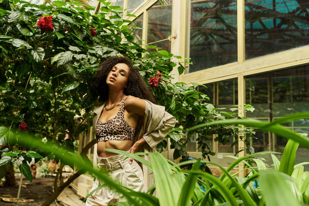 curly african american woman posing with hand on hip in her trendy look in exotic green setting - Foto, afbeelding