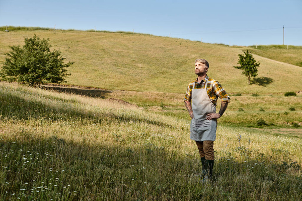 appealing dedicated modern farmer with tattoos and beard relaxing on his farm and looking away - Photo, Image