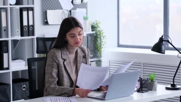 Puzzled Kaukasische jonge Zakenvrouw haalt schouder tijdens het werken met documenten aan het bureau in het kantoor. Evaluatiebegroting, verwarde reactie. - Video