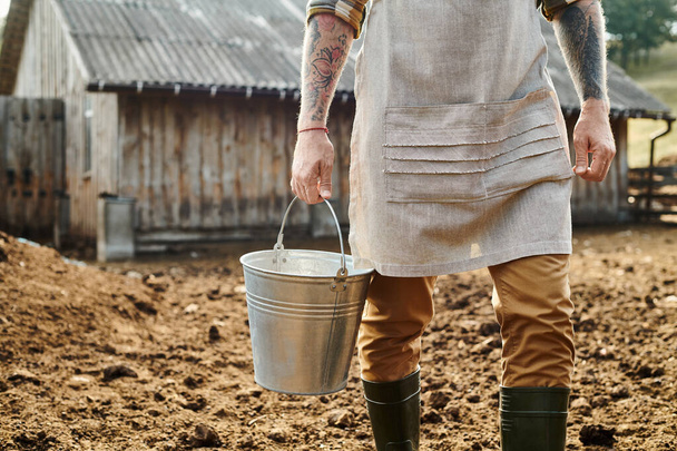 農場でミルクとバケツを保持する腕にタトゥーを入れられた大人の専用男性のクロップビュー - 写真・画像