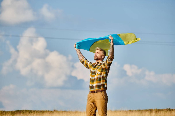 appealing Ukrainian man in casual attire posing with national flag, scenic landscape, modern farmer - Photo, Image