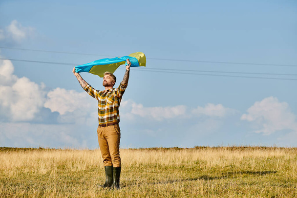 attraente uomo ucraino in abbigliamento casual posa con bandiera nazionale, paesaggio panoramico, agricoltore moderno - Foto, immagini