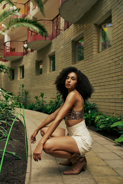 Confident black woman in chic style attire and boots posing in atrium with botanical backdrop - Valokuva, kuva