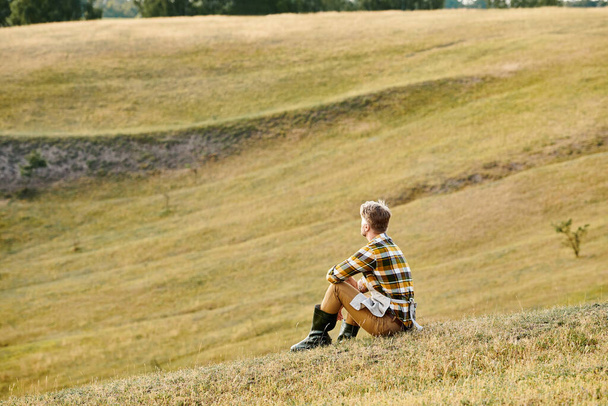 όμορφος αφοσιωμένος άνθρωπος με γενειάδα χαλαρώνοντας στο πράσινο πεδίο της άνοιξης και κοιτάζοντας μακριά, σύγχρονο αγρότη - Φωτογραφία, εικόνα