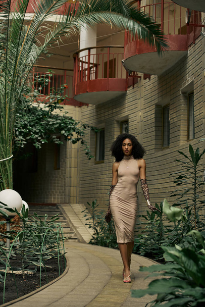Sophisticated african american woman in dress and animal print gloves walking in urban garden - Fotografie, Obrázek