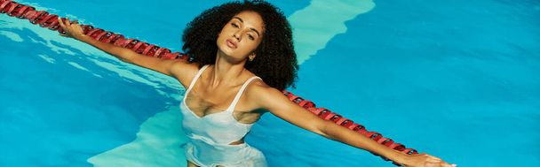 giovane e riccia donna afroamericana nuotare in acqua blu della piscina e guardando la fotocamera, banner - Foto, immagini