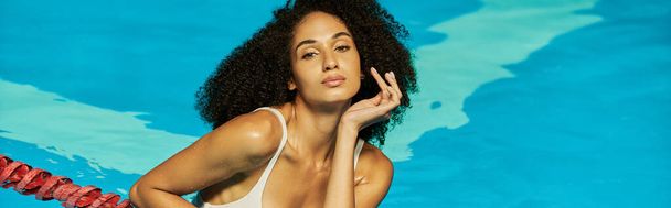 sensual and curly african american woman posing in blue water of swimming pool, banner - Fotó, kép