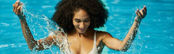 banner of african american woman splashing water in pool, reveling her joy and fun during vacation - Foto, afbeelding