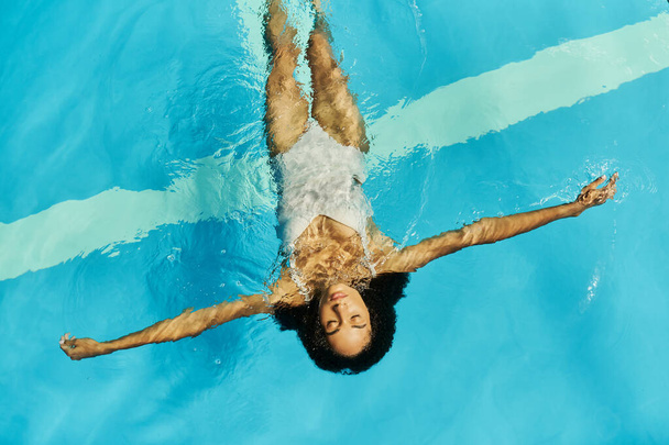 top view of young african american woman swimming on her back in clear pool water, serene and peace - 写真・画像