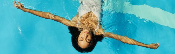 Вид сверху на молодую африканскую женщину, плавающую на спине в чистой воде бассейна, баннер с надписью Serenity - Фото, изображение
