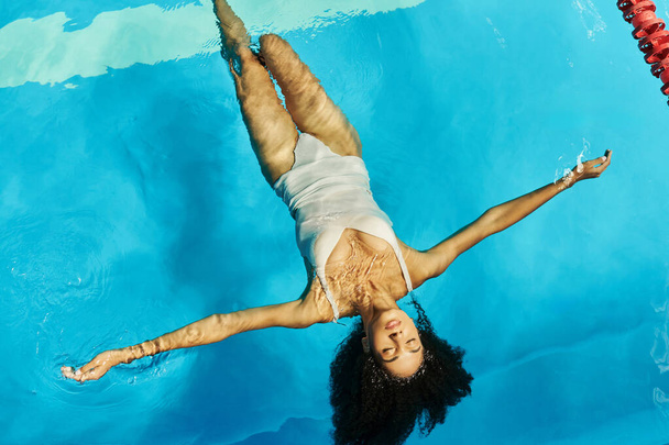 top view of peaceful african american woman swimming on her back in clear pool water, tranquility - Photo, Image