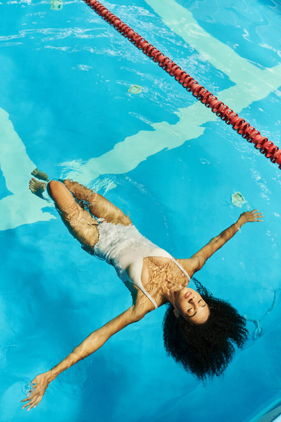 top view of relaxed african american woman swimming on her back in clear pool water, tranquility - Фото, зображення