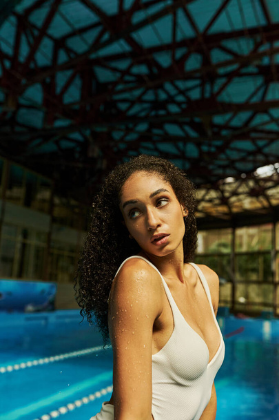 zrelaksowana młoda Afroamerykanka z mokrymi kręconymi włosami i skórą stojąca przy basenie, spokój - Zdjęcie, obraz