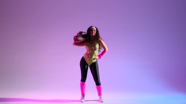 Nerdy žena v retro ansámblu, tančí na zářivém purpurovém pozadí. Držet se za ruce, klasický boombox, zesilující atmosféru výbuchem retro energie. - Záběry, video