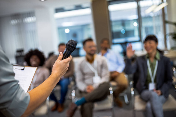 Joven mujer de negocios dando conferencias a sus colegas multiétnicos. Tener un discurso mientras sostiene un micrófono. - Foto, Imagen