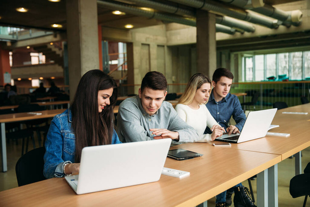 Grupo de estudantes universitários que estudam na biblioteca da escola, uma menina e um menino estão usando um laptop e se conectando à internet
. - Foto, Imagem