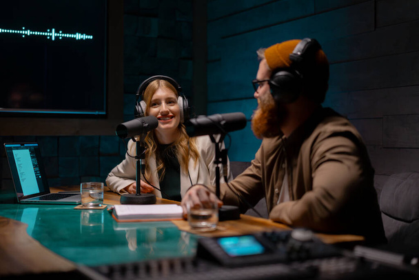 Fröhliche junge stilvolle Radiomoderatoren nehmen frische Podcast-Episoden im Loft-Studio auf. Attraktive, energische Co-Moderatoren diskutieren wichtige Themen live auf Sendung in einer Abendshow - Foto, Bild