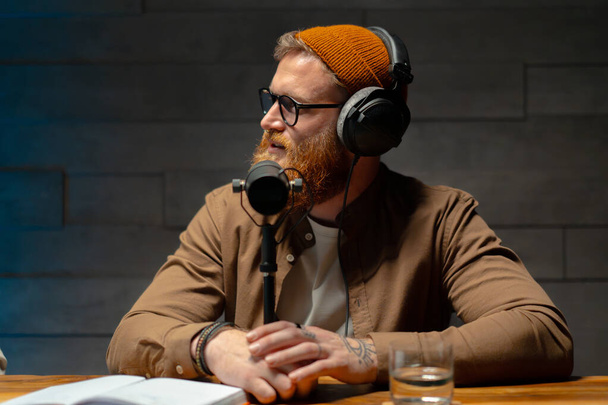Maschio podcaster intervistare un ospite in uno studio di registrazione. ragazzo barbuto seduto a tavola con computer portatile e microfono - Foto, immagini